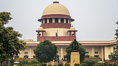 Supreme Court building in India with a statue in front and lush greenery around.