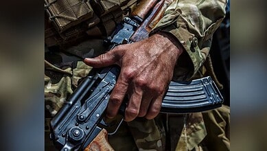 Close-up of a soldier's hand holding a rifle in camouflage uniform.