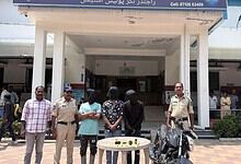 People gathered outside a building in Hyderabad, some in uniform, with a table and motorcycle in front.