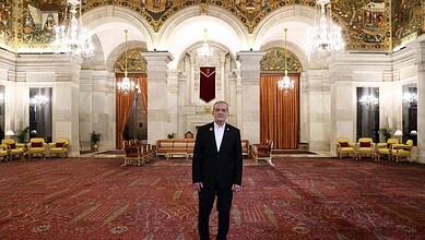 Pezeshkian standing in the grand hall of Rashtrapati Bhavan with ornate ceiling and chandeliers.