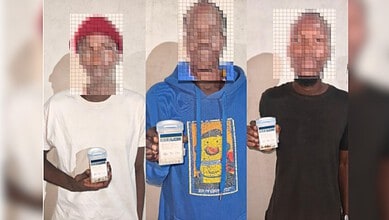 Three men holding mobile phones, image pixelated, in front of a plain background.