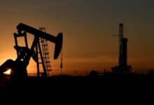 Silhouette of an oil pumpjack and drilling rig at sunset in an oil field.
