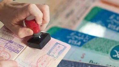 A close-up of a hand stamping a passport, with Saudi Arabian visa documents visible in the background.