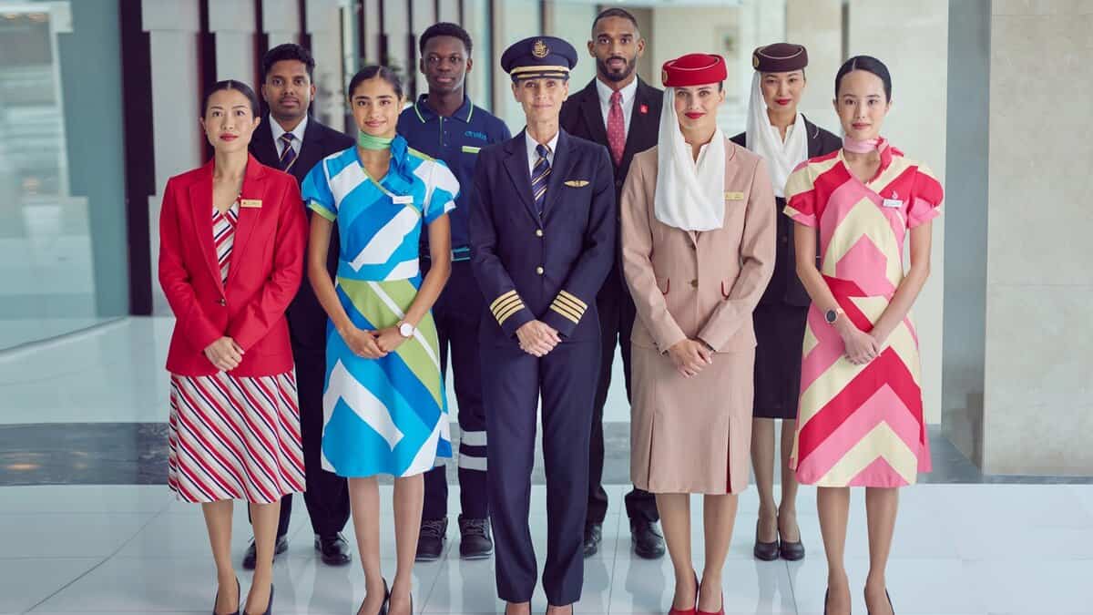A group of Emirates airline staff in diverse uniforms standing together in a modern indoor setting.