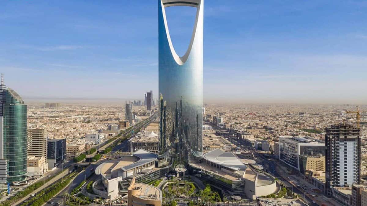 Aerial view of the Kingdom Centre Tower, a modern skyscraper with a distinctive glass design and skybridge, standing prominently in Riyadh's urban skyline, surrounded by contemporary buildings in the desert landscape of Saudi Arabia.