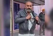 Image shows a man wearing a gray jacket and holding a snake stands in what appears to be a public space