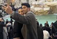 Malaika Arora taking a selfie with a man in Italy, surrounded by tourists and scenic water features.