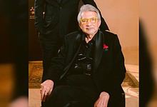 Rajan Lall in black suit with yellow glasses seated indoors at an event.