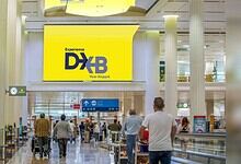 Passengers walking through Dubai International Airport terminal with DXB signage in bright yellow.
