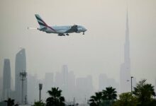 Emirates Airbus A380 approaching landing at Dubai International Airport with Dubai skyline and Burj Khalifa in the background.