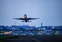Airplane taking off from runway at dusk, with city skyline in background.