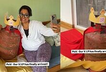 A woman holding a phone and smiling next to a large LPG cylinder with a humorous crown label, highlightin.