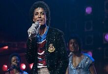 Actress portraying Michael Jackson in a biopic performs on stage with microphone, dressed in iconic style.