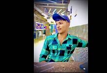 Young man in a blue cap and checkered shirt sitting in a public space, possibly Talabkatta, Hyderabad.