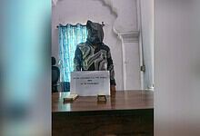 Person with face covered behind a desk with seized counterfeit currency notes, related to counterfeit cur.