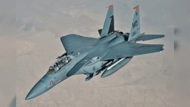 F-15E fighter jet in flight over desert terrain.
