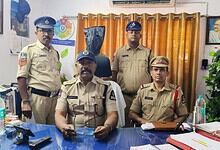 Police officers in uniform posing in an office setting with curtains and framed photographs.