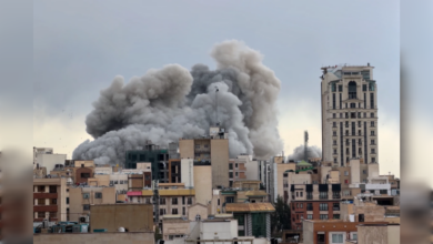 Thick grey smoke billows over buildings in Tehran after an air strike, rising above the urban skyline.
