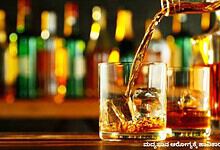 A refreshing glass of whiskey with ice cubes, with colourful bottles blurred in the background.