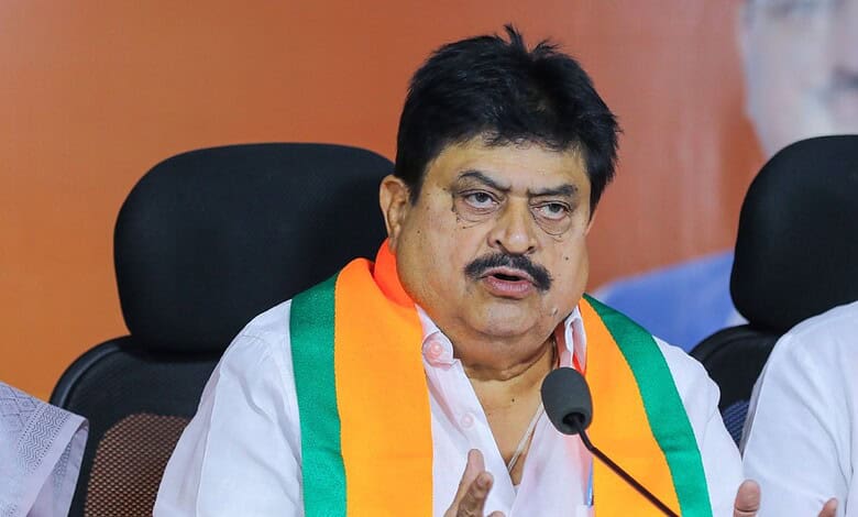 A man speaking at a press conference, wearing a white shirt and a tricolour sash, with a serious expressi.