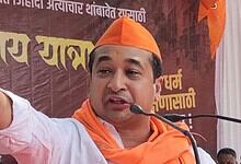 Prominent Indian politician speaking at a public event, wearing orange attire and cap, with a microphone,.