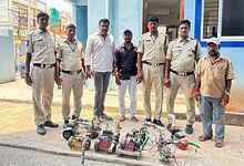 Suspected illegal water pump operators detained by police officers in front of a colourful building.