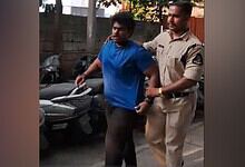 A man in a blue shirt being escorted by a police officer on a street.