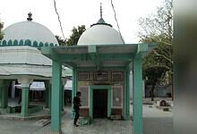 Ancient Hindu temple with domed structures and green pillars, surrounded by trees, in a peaceful outdoor.