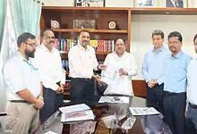Senior officials and executives in a formal meeting exchanging documents in an office setting.