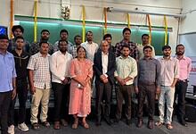 Group of university students and faculty members posing together at an academic event, with a green chalk.