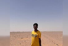 Young man standing in a vast, arid desert landscape under a clear blue sky.