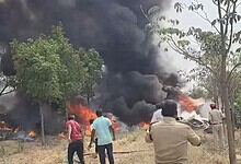 Vehicle on fire with thick black smoke during an outdoor incident, surrounded by trees and onlookers in t.