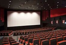 A nearly empty movie theatre with a large blank screen and rows of red and black seats.