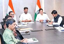 India government officials in a meeting with Indian flags in the background.