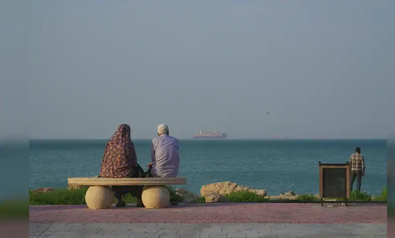 Two people sitting on a bench by the sea, with a ship in the distance, illustrating US military activity.