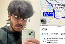 A young man with dark hair and glasses taking a selfie with a smartphone, standing outdoors on a cloudy d.