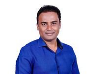 A smiling man in a blue shirt posing for a professional photo for The Siasat Daily.