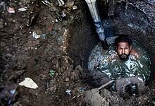 Man trapped in a deep, narrow sewer well with water up to his chest.