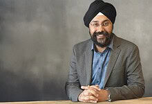 Prabhjeet Singh smiling in a grey blazer and blue shirt against a grey background.