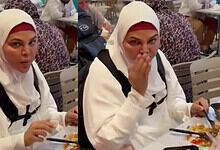 Woman in white hijab covering her head, eating food at a crowded restaurant table.