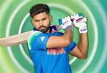 Cricketer holding a bat and wearing gloves, ready to play cricket, against a vibrant green background.