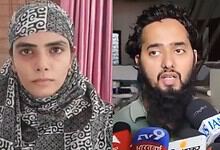A woman wearing a patterned headscarf and a man with a beard speaking to the media with multiple micropho.