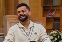 Smiling man with a beard in a cream shirt sitting in a wooden room.