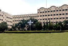 Large government or institutional building with a well-maintained lawn and palm trees in front.