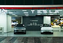 Tesla showroom displaying two electric cars inside with a modern interior and branding.