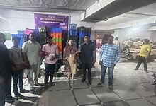Group of people standing in Zepto warehouse with expired food items in the background.