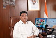 Official portrait of a man in a white shirt sitting at a desk in an office.