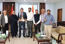 Group of men in formal attire at a meeting, with one man receiving a cake, in Hyderabad.