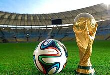 FIFA World Cup football and trophy on a stadium field under bright sunlight.