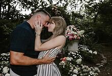 A couple in love touching foreheads in a garden with blooming flowers and greenery.